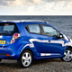A photo of a blu Chevrolet Spark parked on a beach.